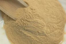 A close-up of light brown powder in a white bowl with a small wooden scoop.