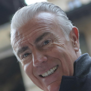 Smiling man with gray hair in a dark jacket.