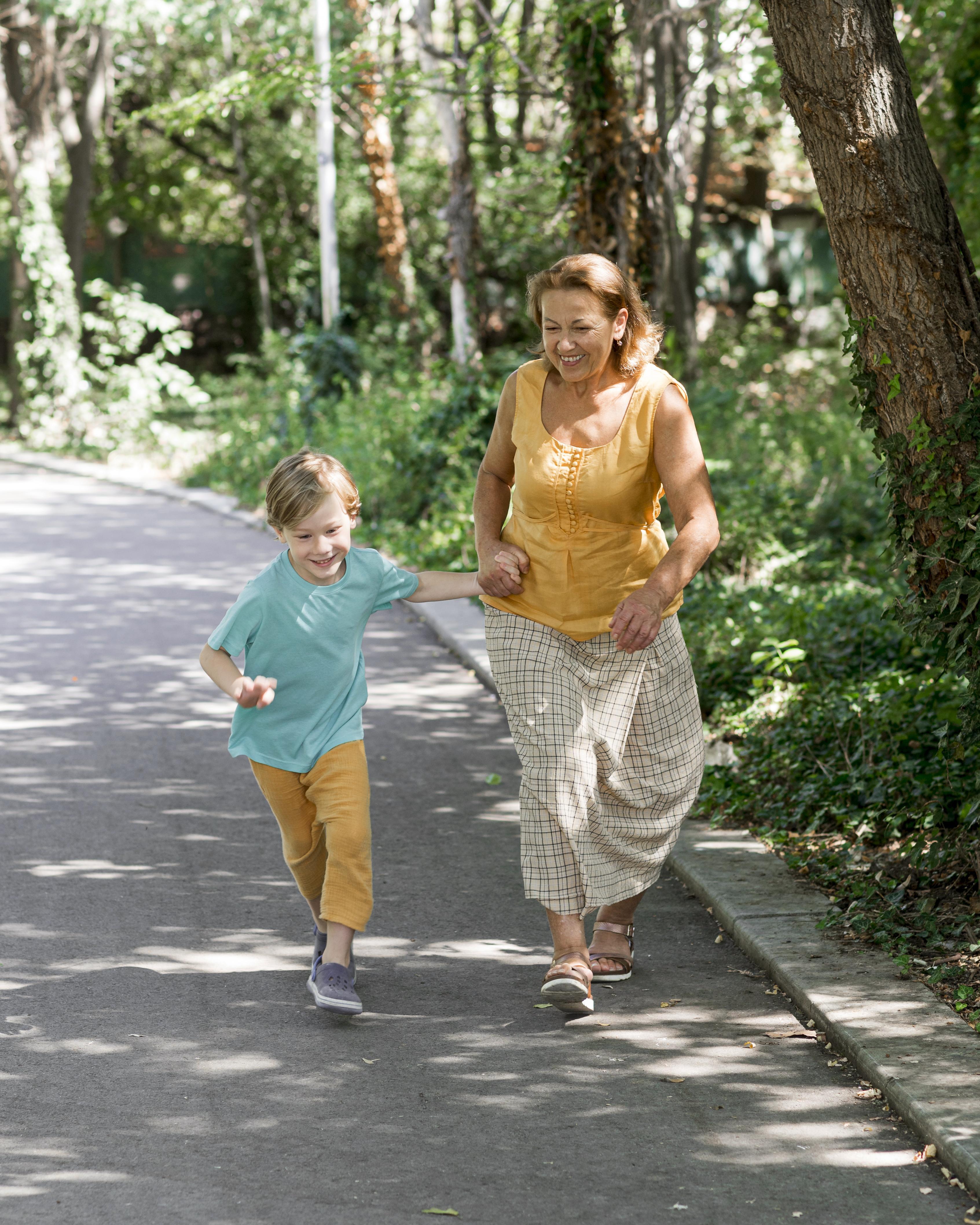 A woman and child walking and smiling on a tree-lined path.
