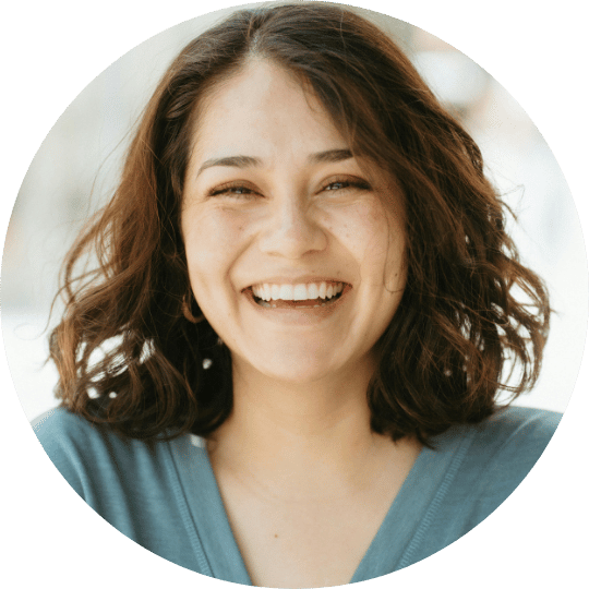 A circular headshot of a smiling woman with wavy brown hair, wearing a blue shirt.