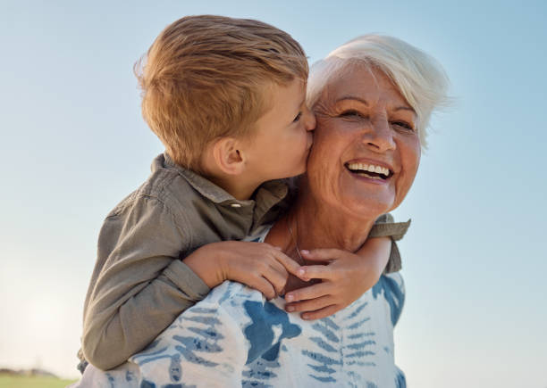 Child kissing an elderly woman on the cheek, both smiling outdoors.