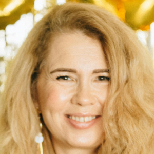 Smiling person with long blonde hair and a blurred background.
