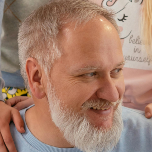 A smiling man with a gray beard, wearing a light blue shirt.