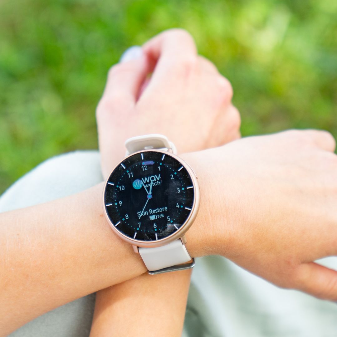 A close-up of a person's wrist wearing a WAV smartwatch with a white band outdoors.