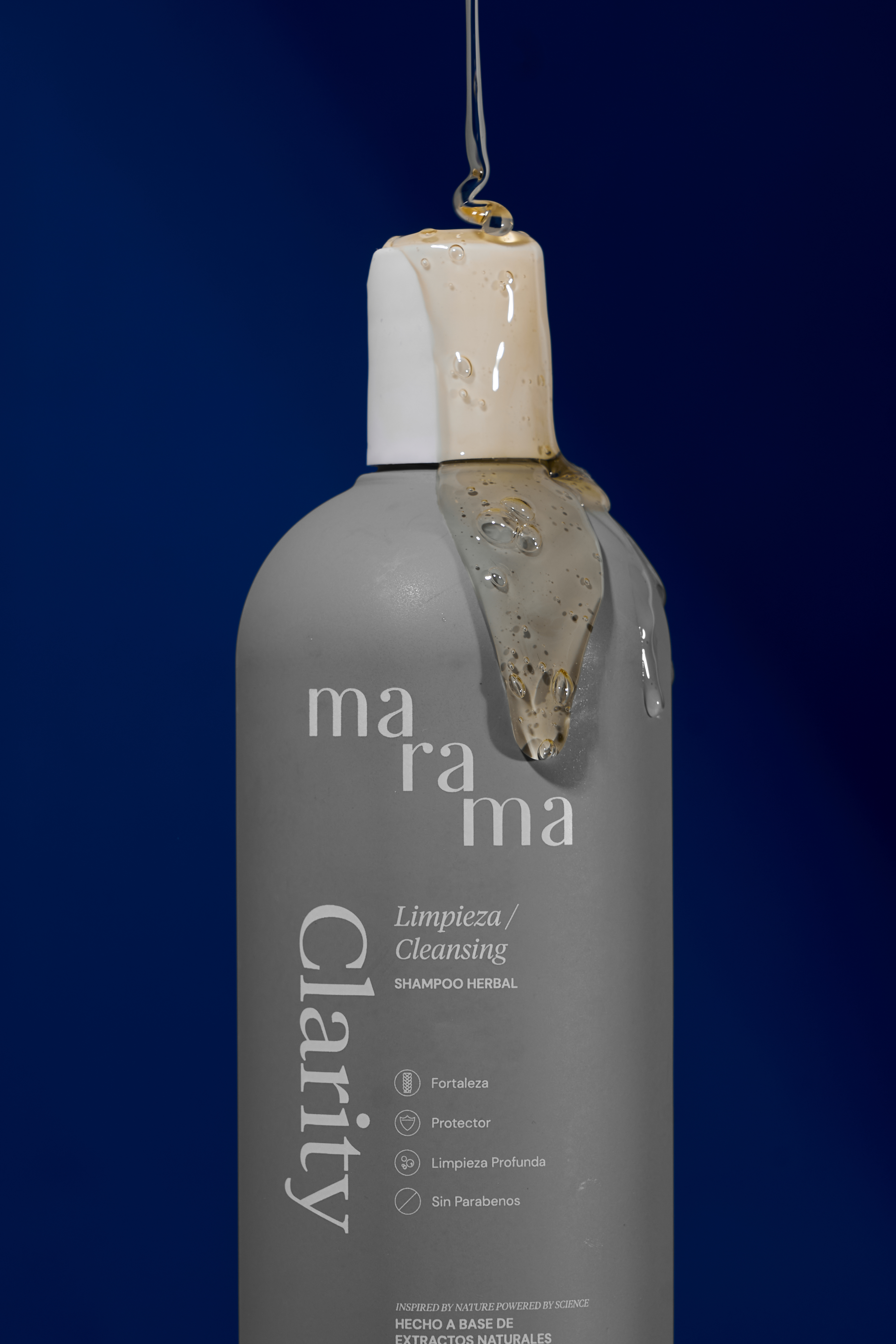 Gray shampoo bottle with liquid pouring over the cap, against a blue background.