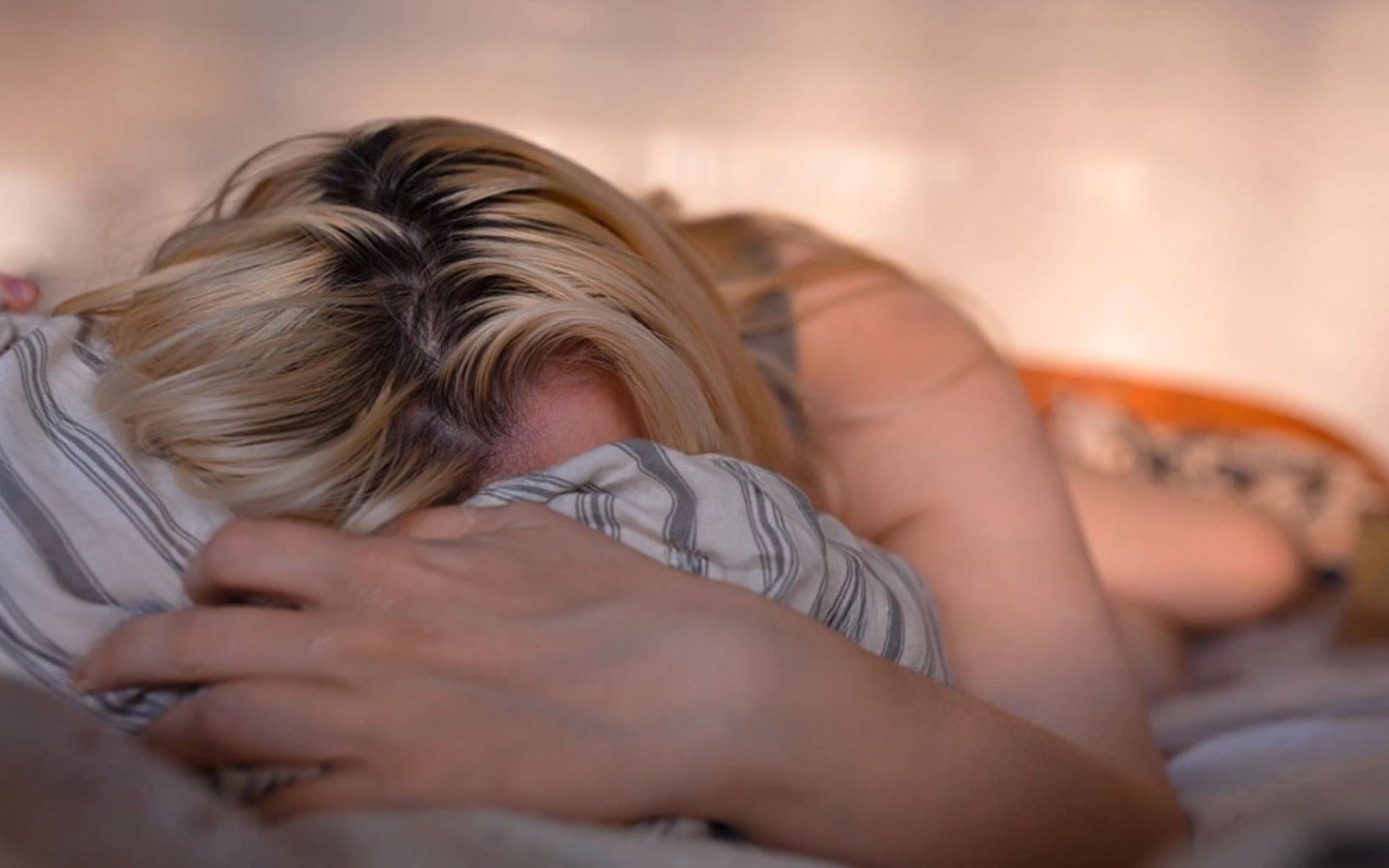Person lying face down on a bed with striped pillow cover.