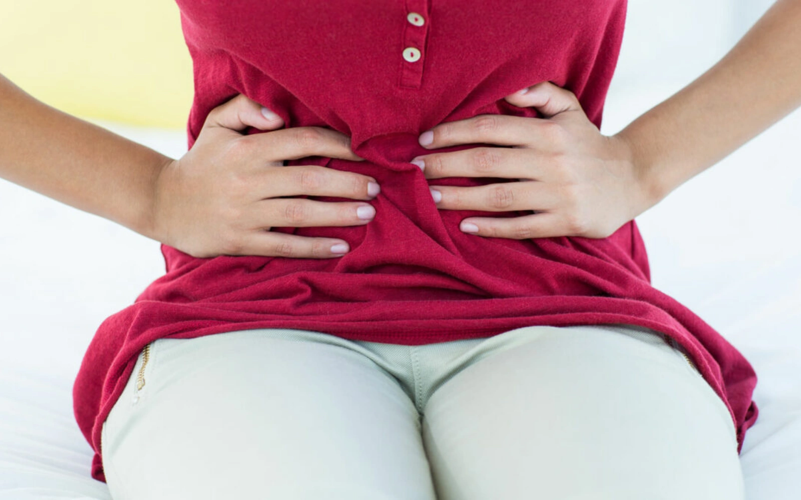 Person holding stomach with both hands, wearing a red shirt.