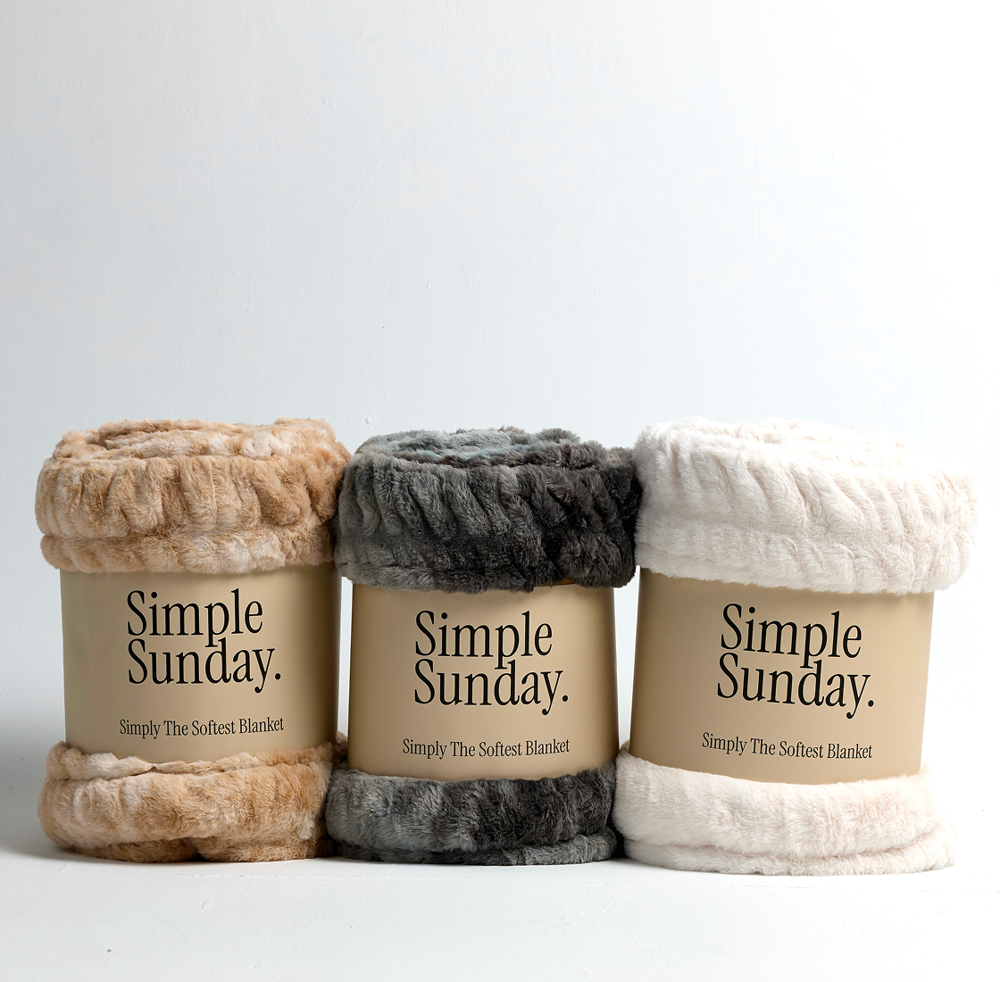 Three rolled blankets in beige, grey, and white with 'Simple Sunday' labels.
