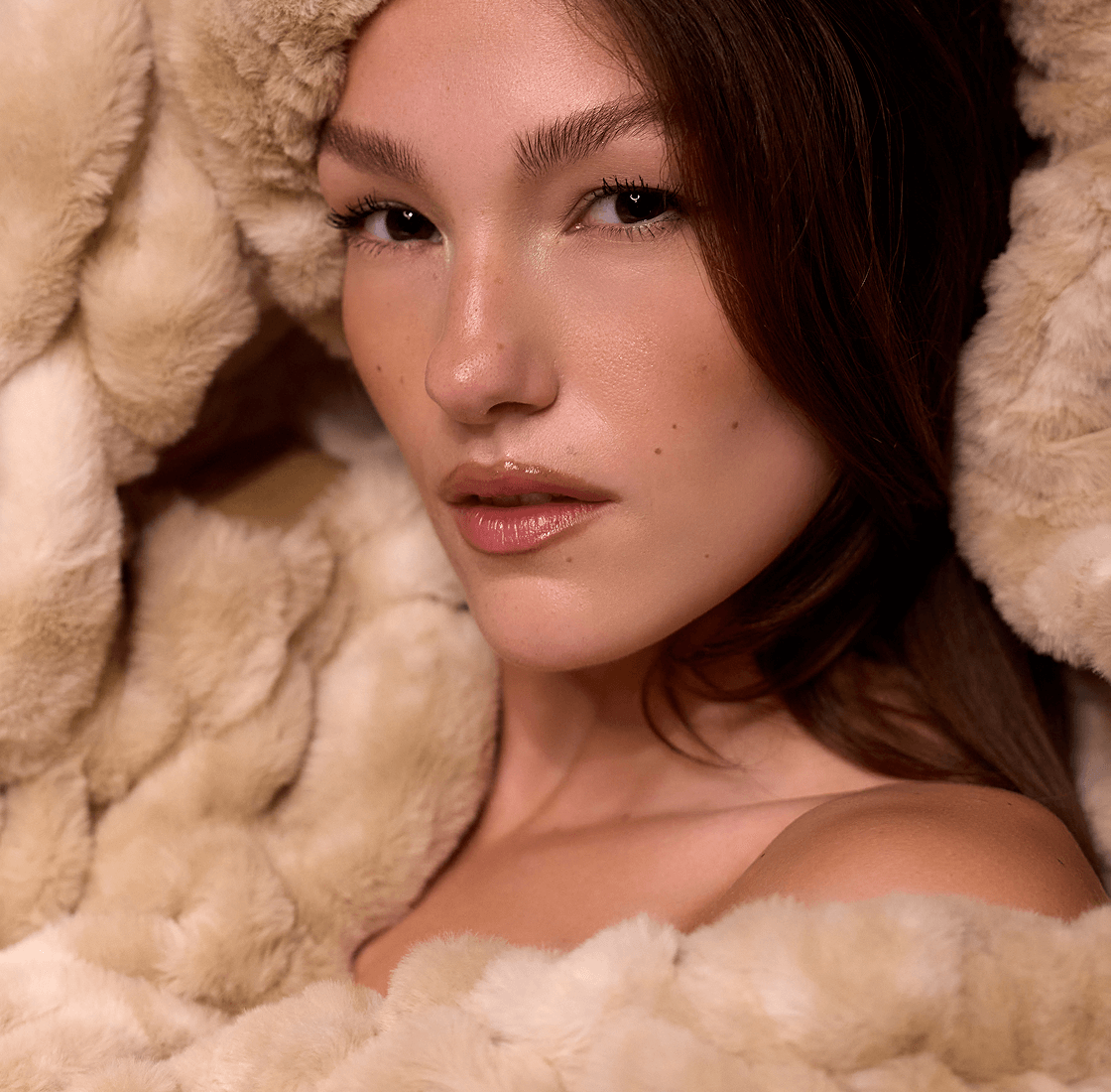 Person wrapped in soft, beige fur, looking directly at the camera.