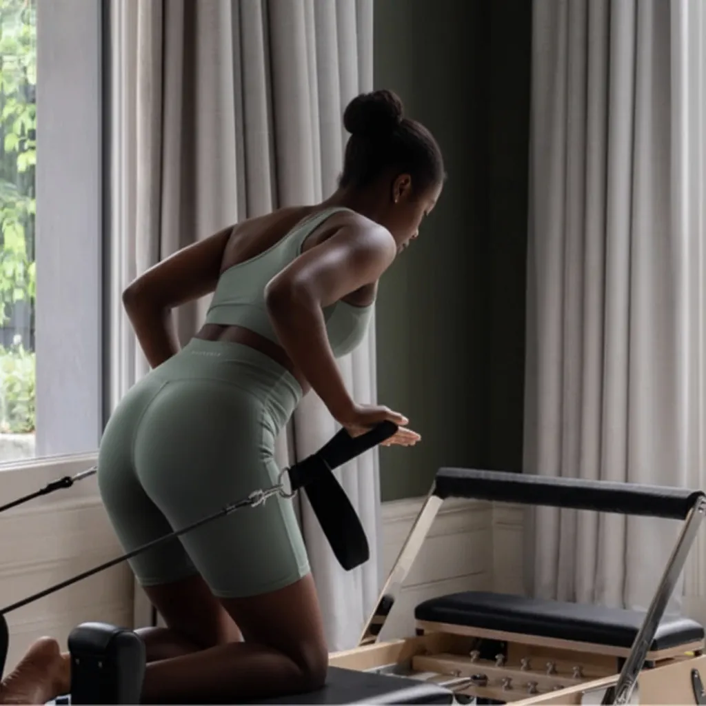 Person exercising on a pilates reformer near a large window.