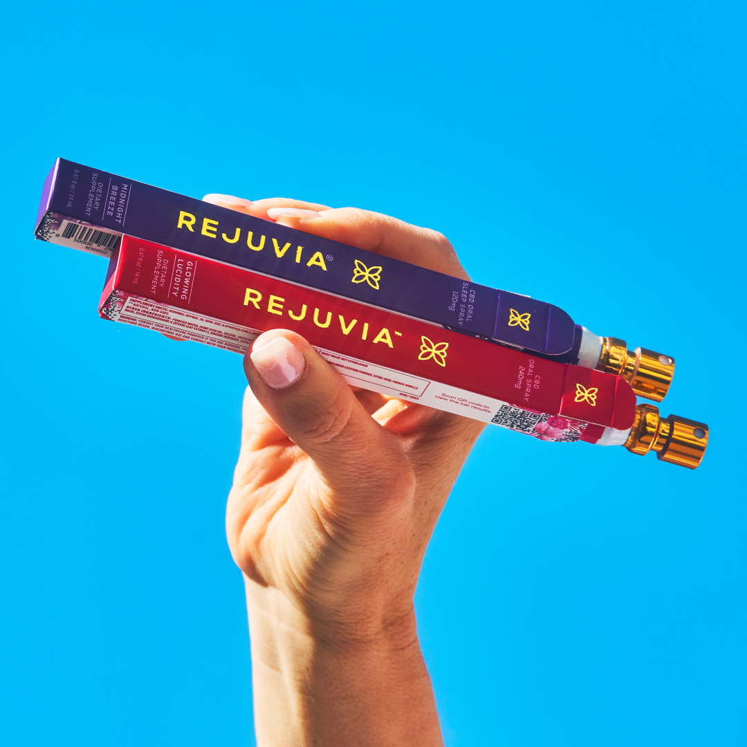 Hand holding two Rejuvia CBD oil spray boxes against a clear blue sky.