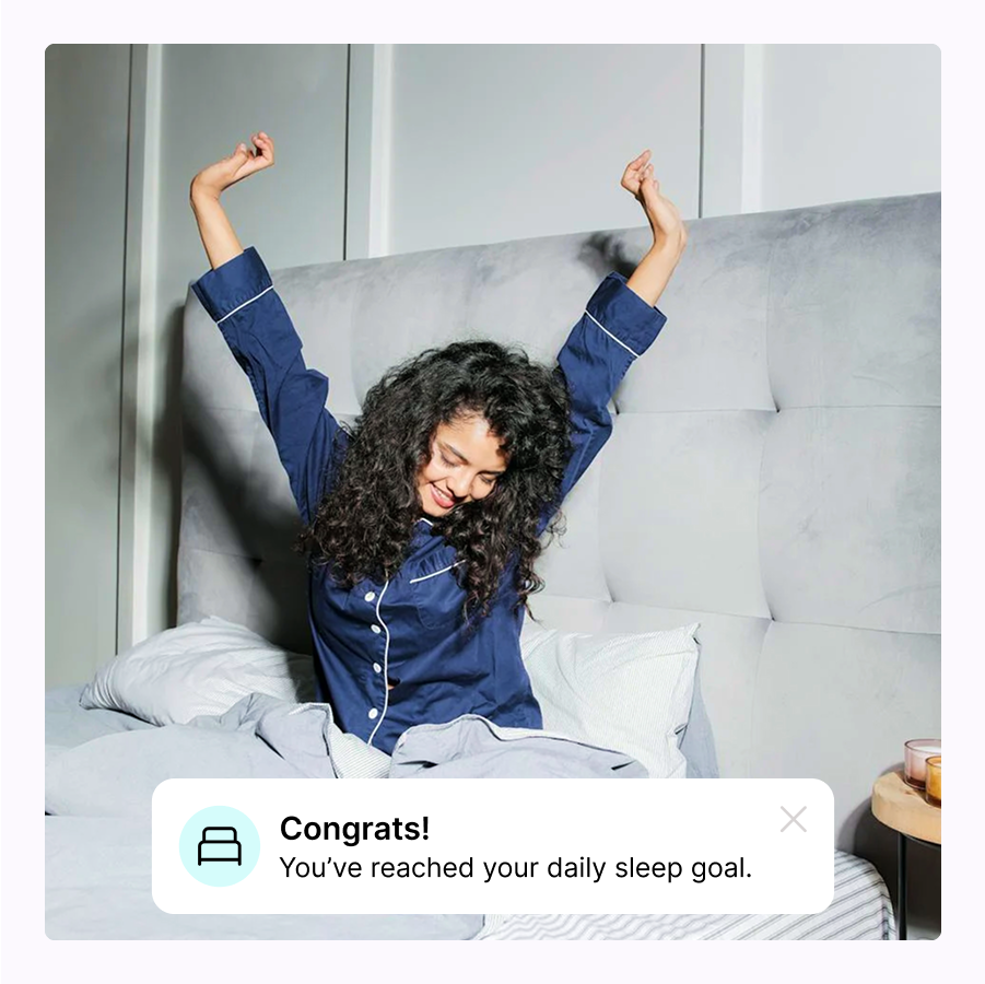 Person in bed stretching, wearing blue pajamas, notification about sleep goal met.
