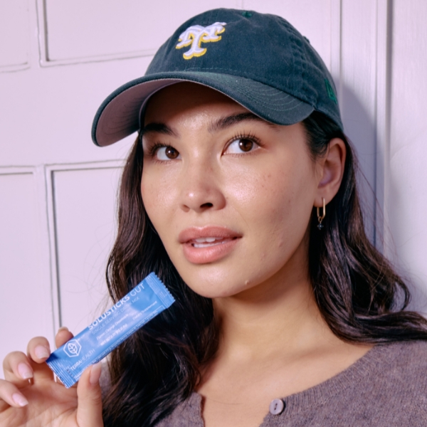 Person wearing a cap holding a blue product packet.