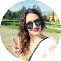 Person outdoors making a peace sign with sunglasses and a park background.
