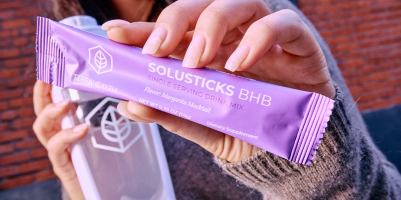 Person holding a purple Solusticks BHB drink mix packet.