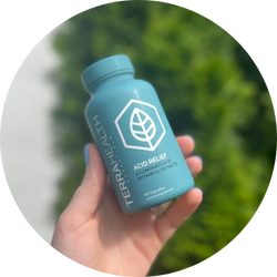 Hand holding a blue bottle labeled 'Terra Health Acid Relief' against a blurred green background.