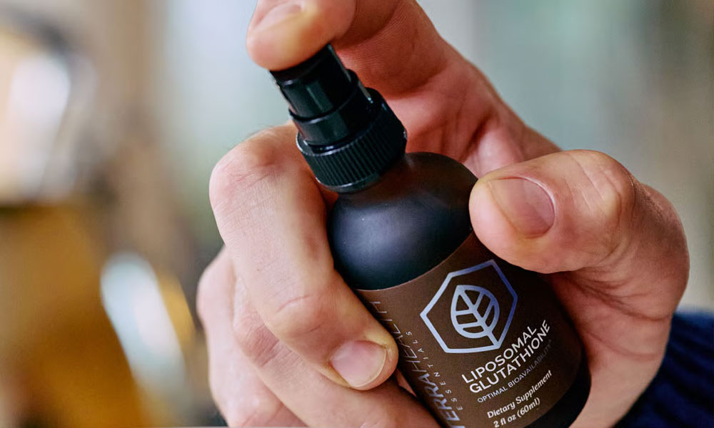 A person's hand holds a small, dark spray bottle, with a finger on the pump.