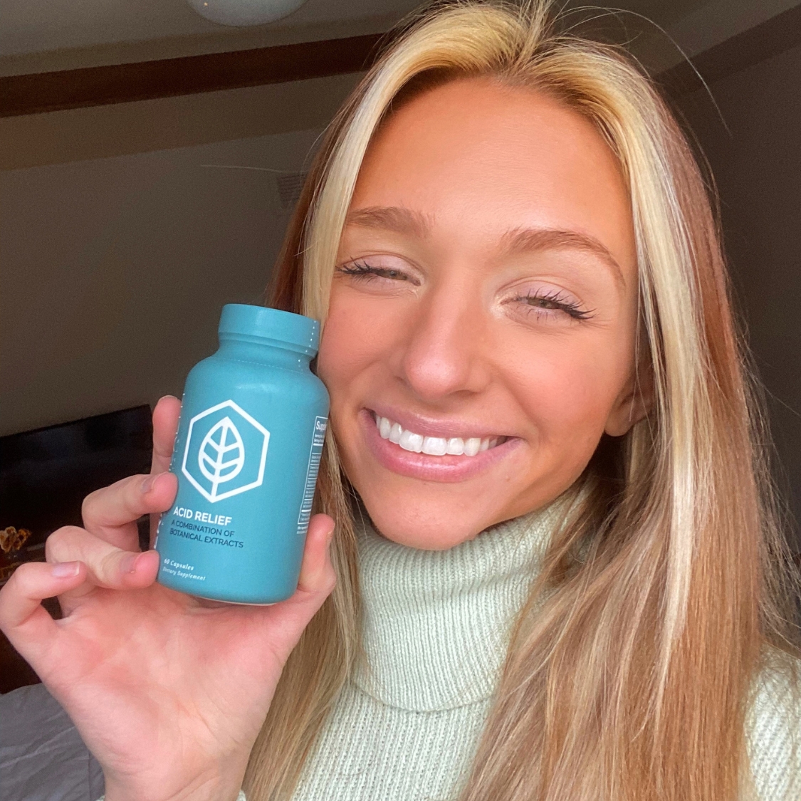 Person smiling and holding a blue bottle with a leaf logo.