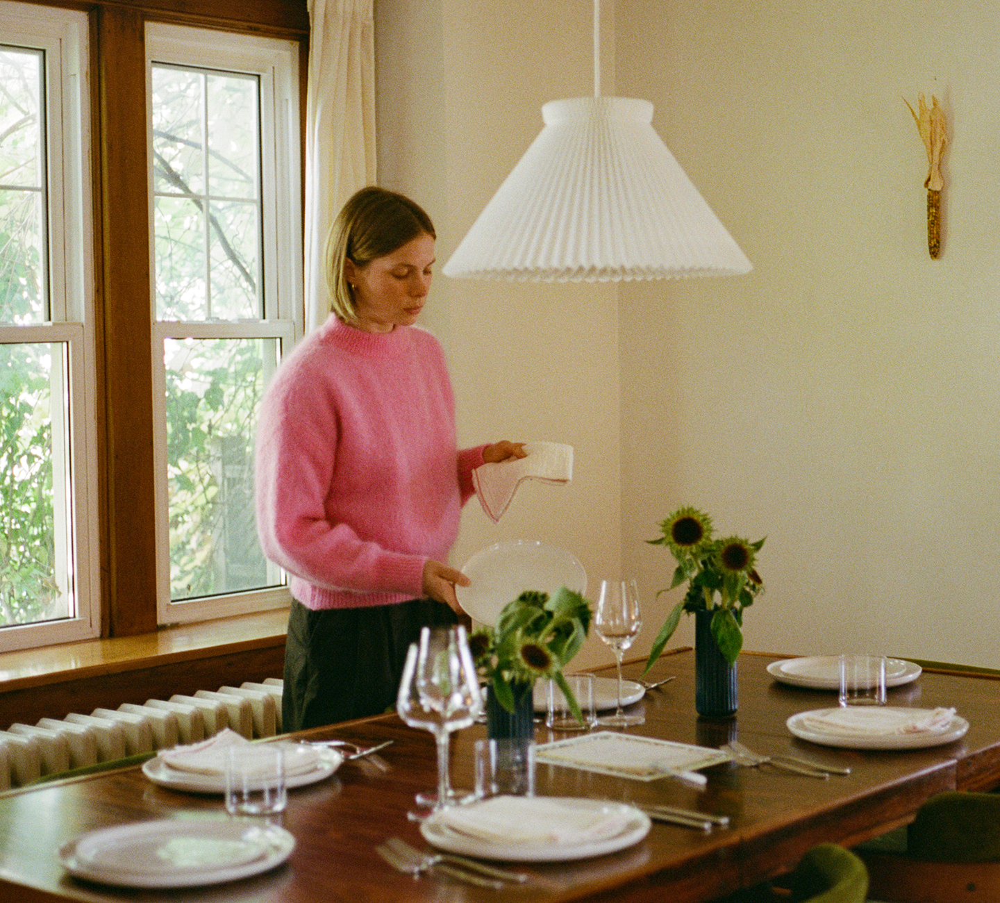 Tess is setting a dining table with flowers and glassware.