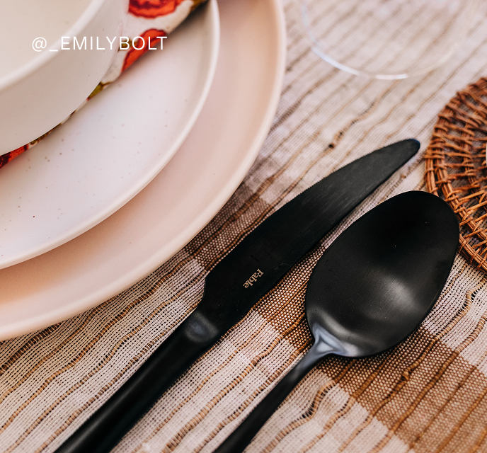 Black knife and spoon beside a white plate on a striped cloth.