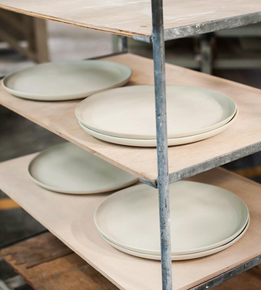 Stacked ceramic plates on wooden shelves in a workshop.