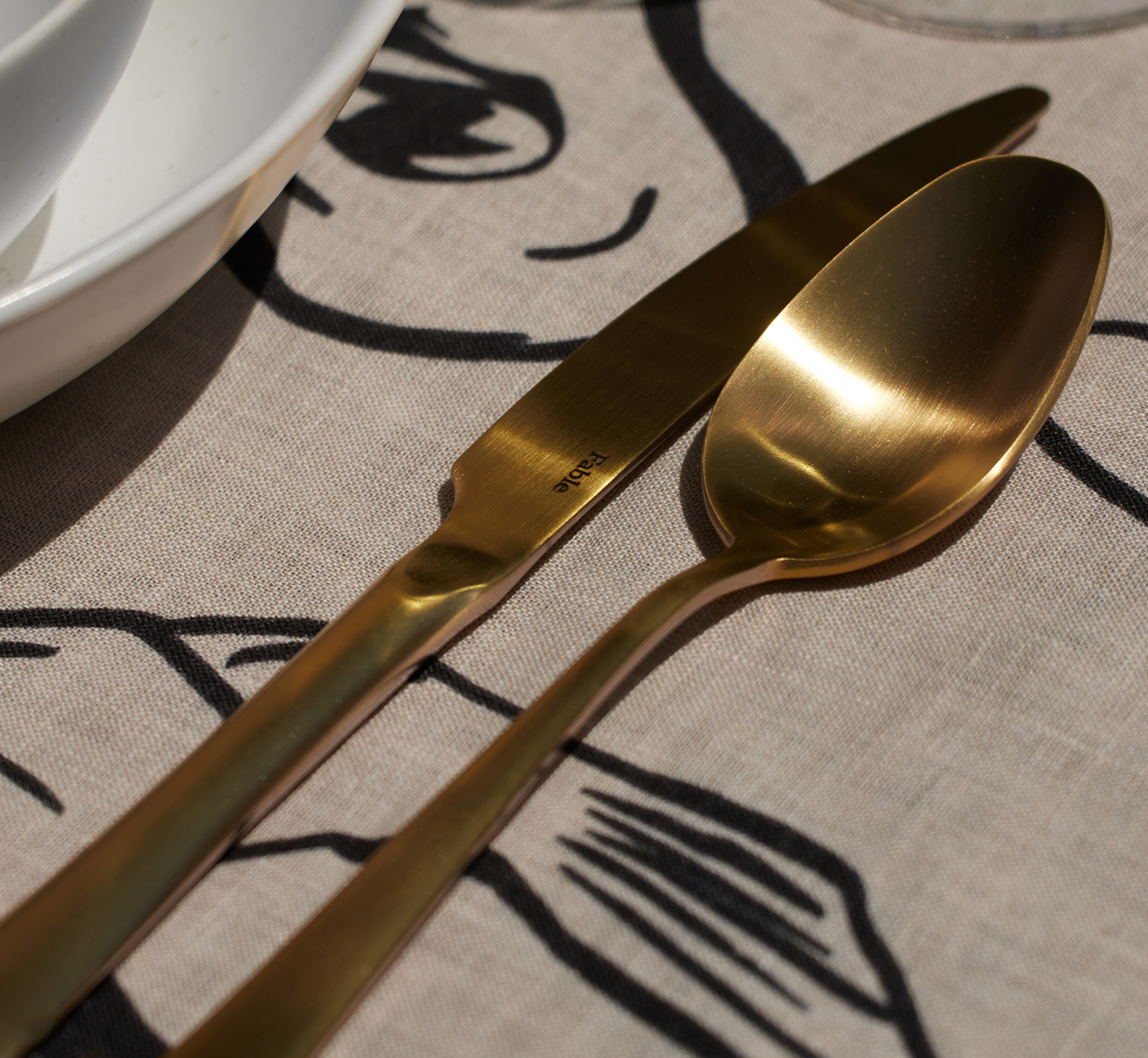 Gold knife and spoon on a patterned tablecloth.