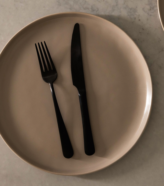 A black fork and knife on a beige plate.