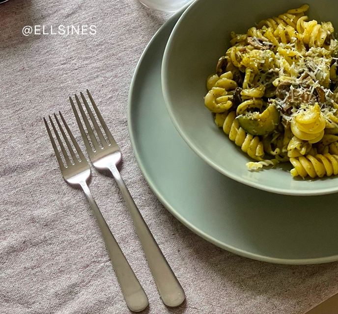 Plate of pasta with grated cheese next to two forks on a tablecloth.