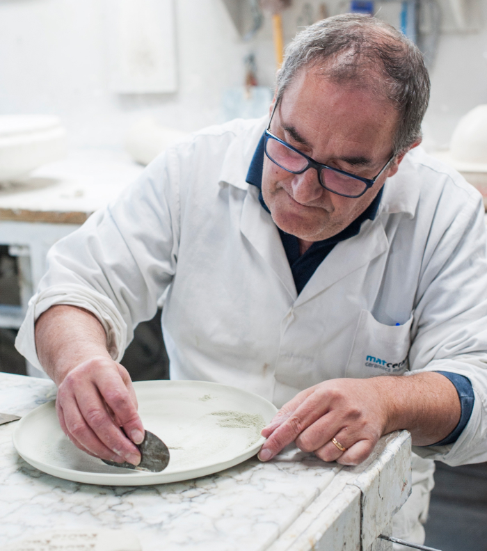Man in a lab coat shaping or decorating a ceramic plate
