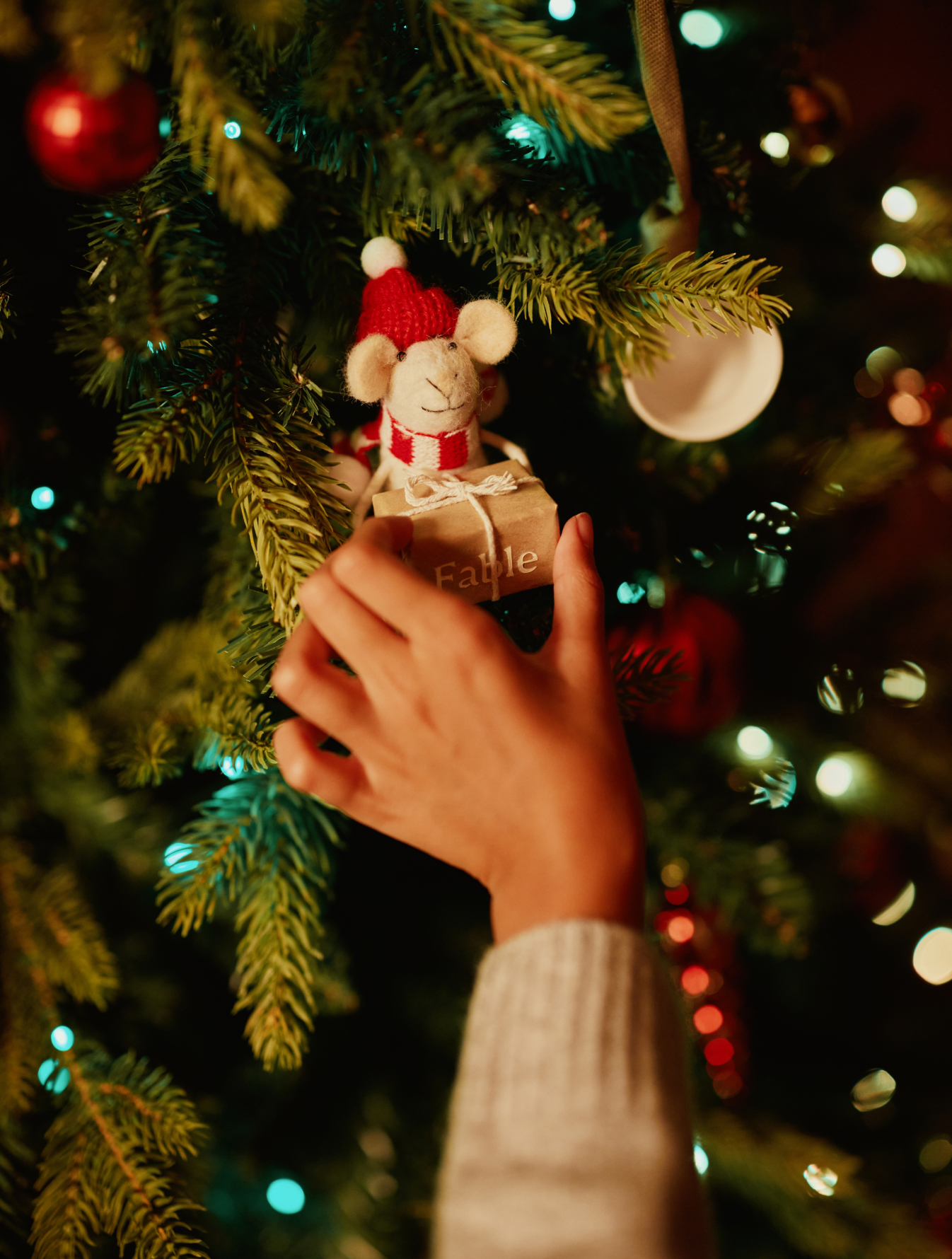 Hand placing a small mouse ornament on a Christmas tree