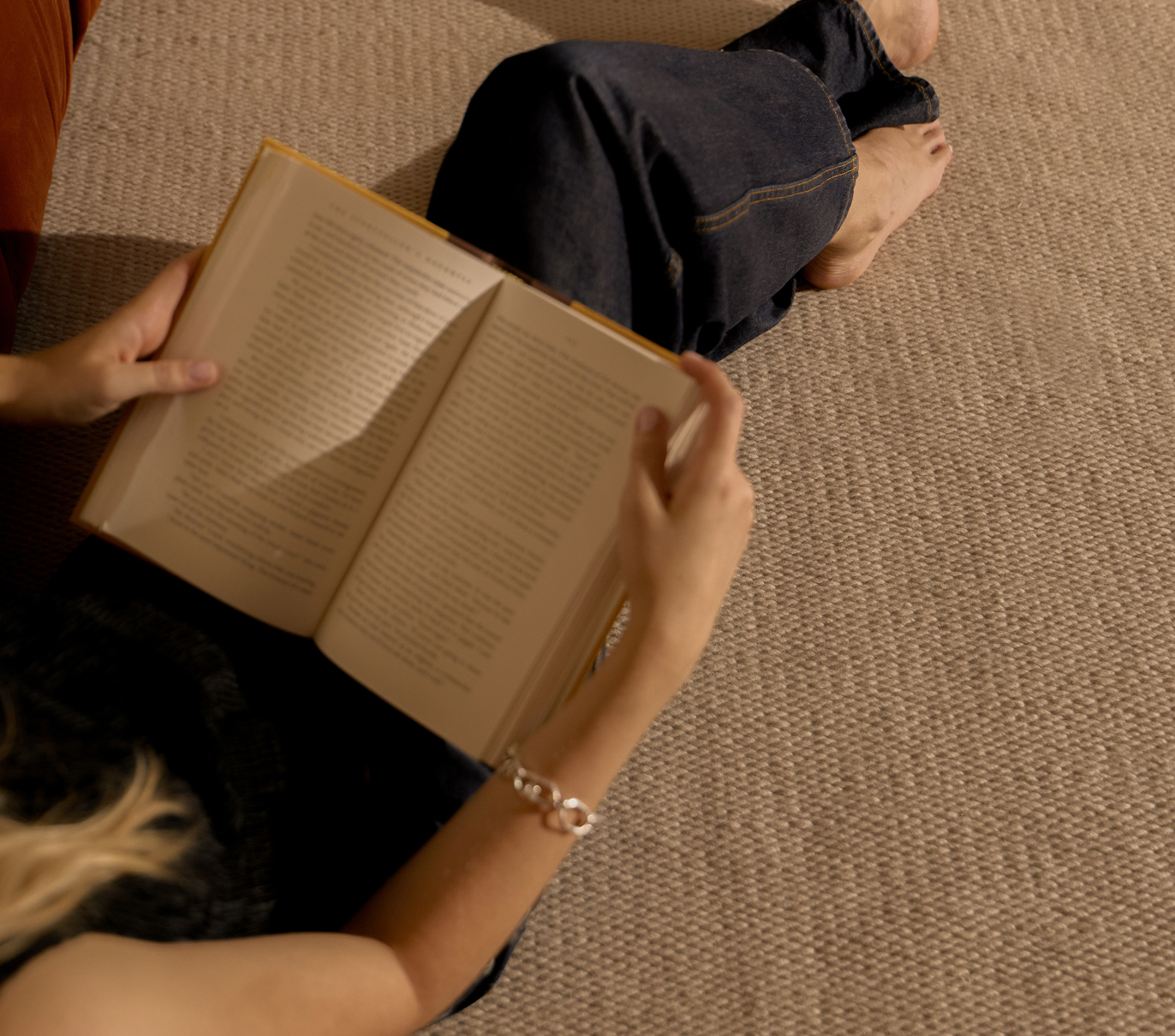 A woman sits on a rug and reads