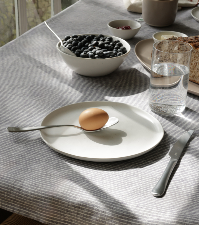 Plate with egg and spoon on table, alongside glass and bowl of blueberries.