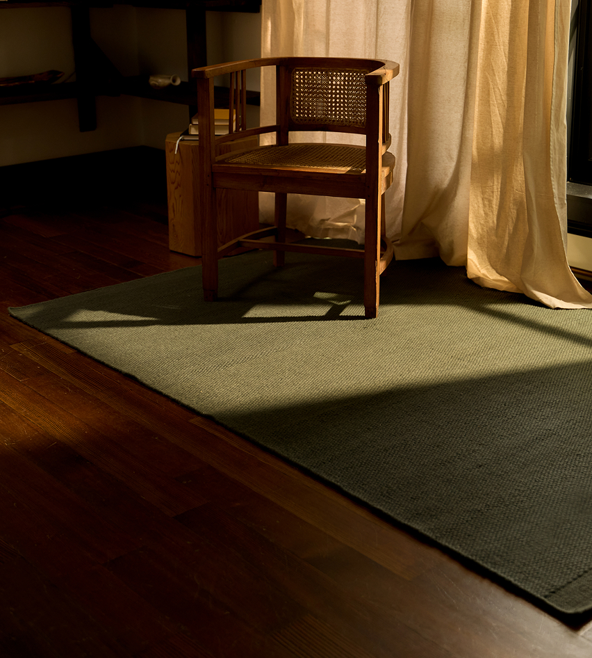 Wooden chair on a rug with sunlight streaming through curtains.