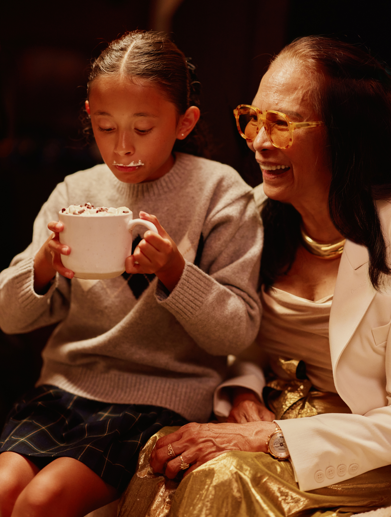 Child drinking hot chocolate while sitting next to a smiling woman
