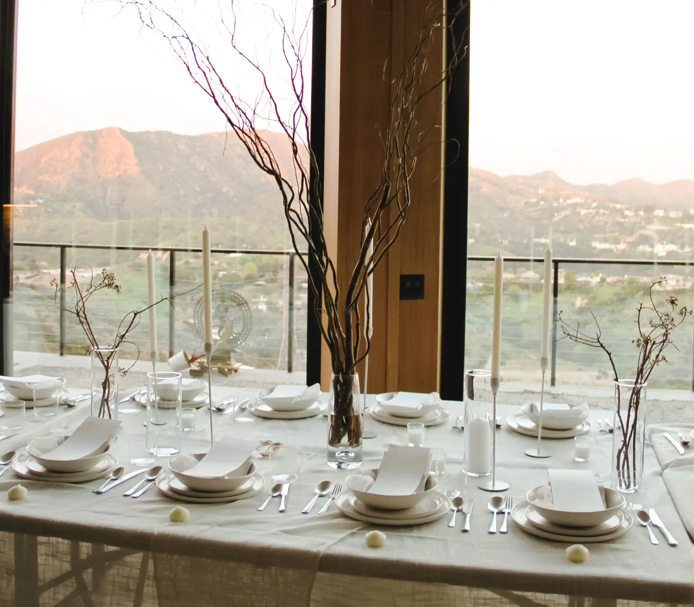 Elegant table setting with white plates, cutlery, and tall candles, overlooking a mountain view.