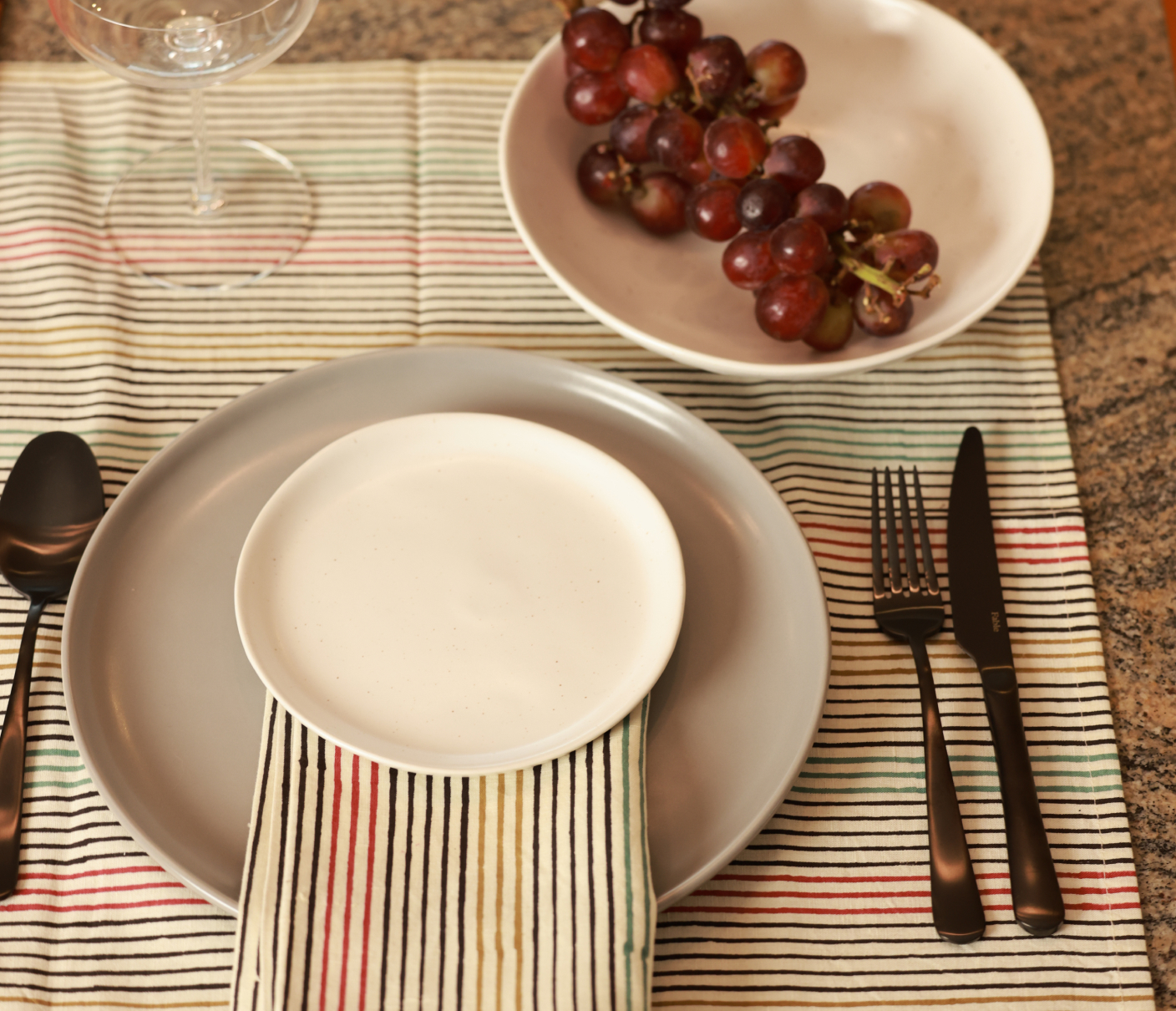 Table setting with plates, cutlery, and a bowl of grapes on a striped cloth.