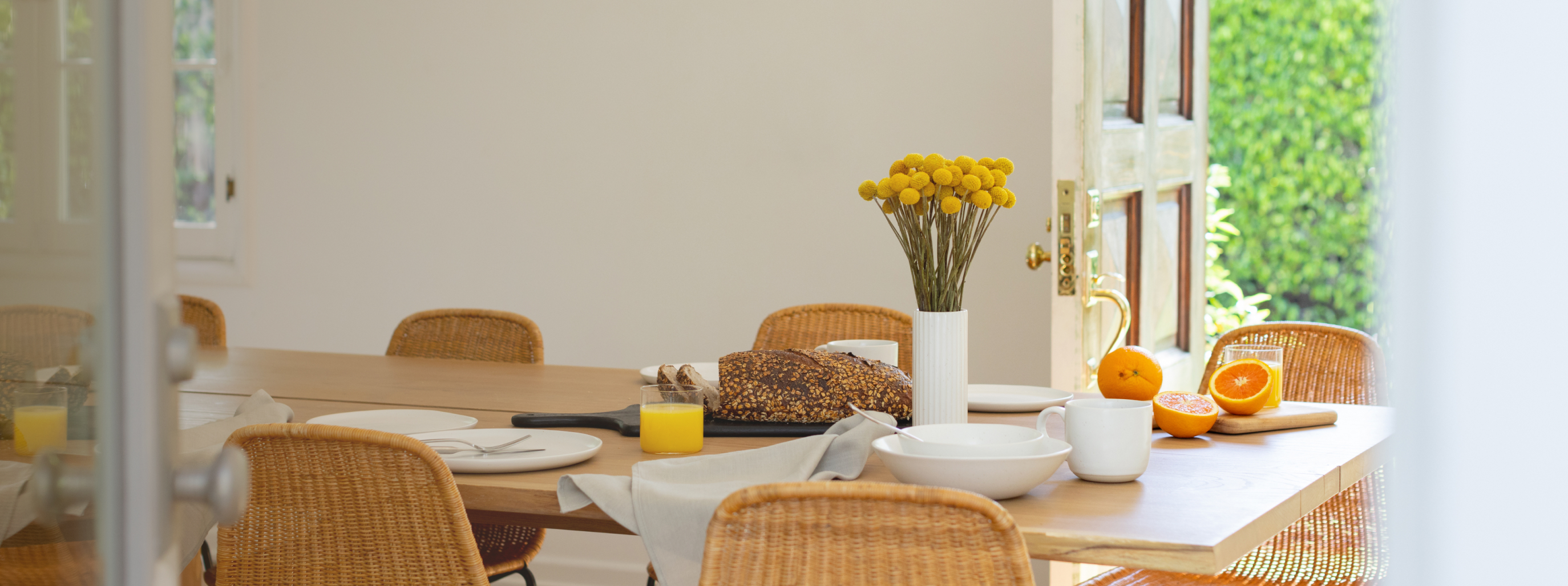 Dining table with flowers, orange juice, bread, and a cut orange.