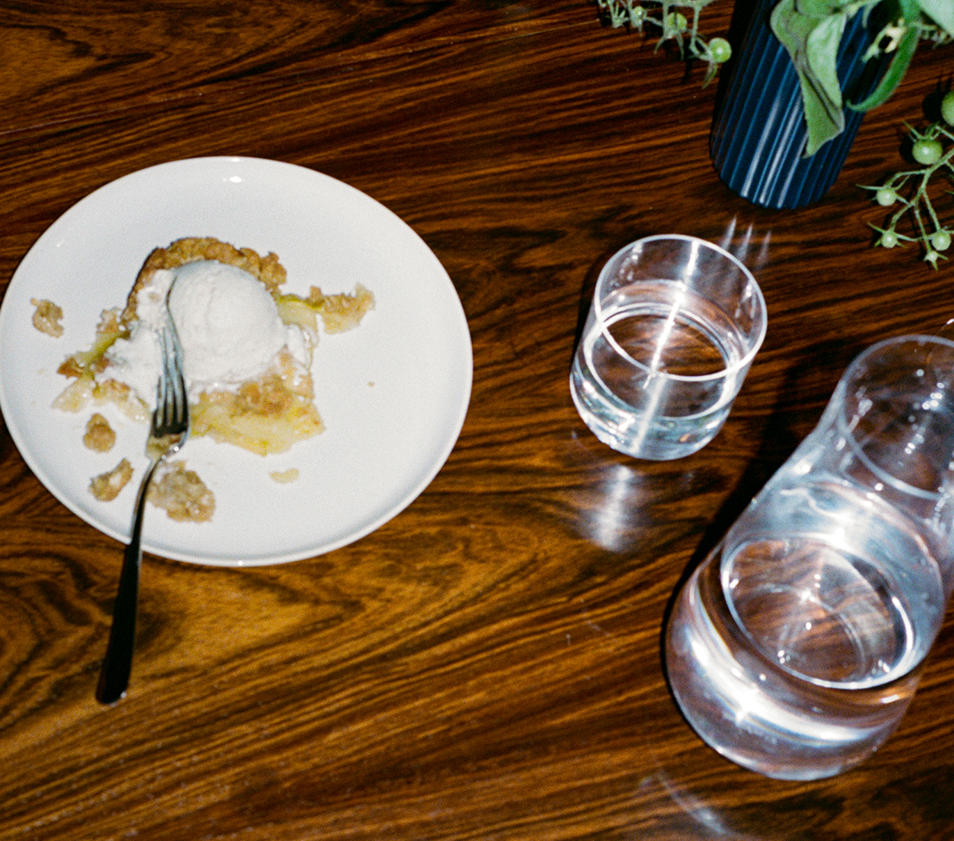 Dessert with ice cream on a plate, glass of water on a wooden table.