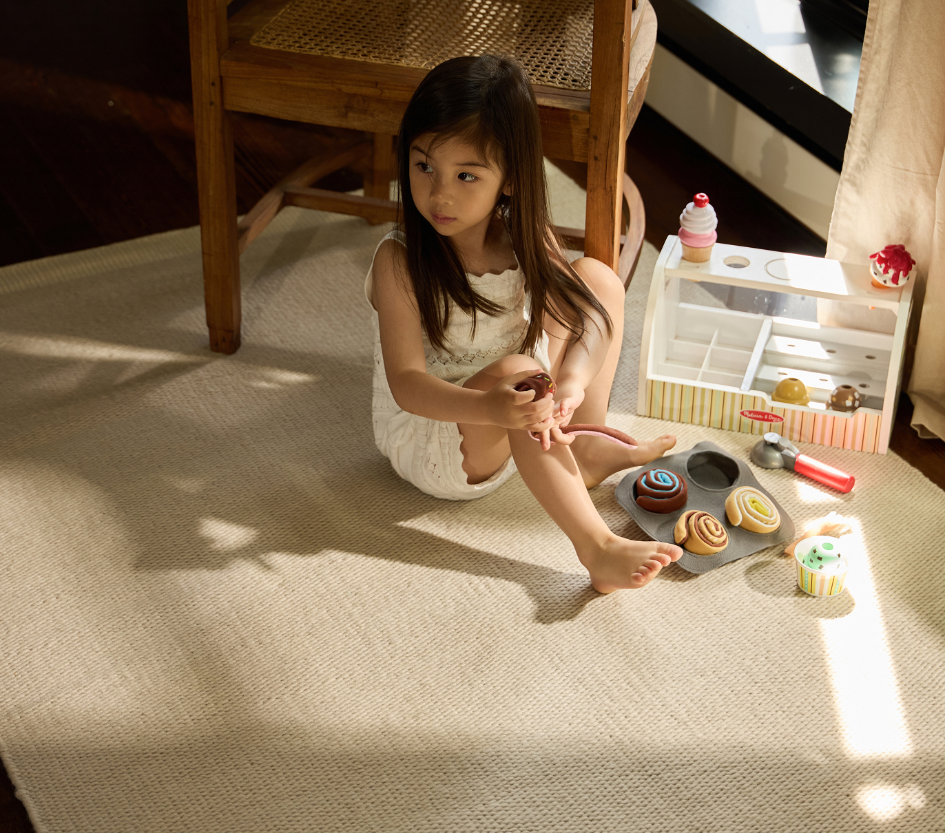 A girl sits on a rug and plays