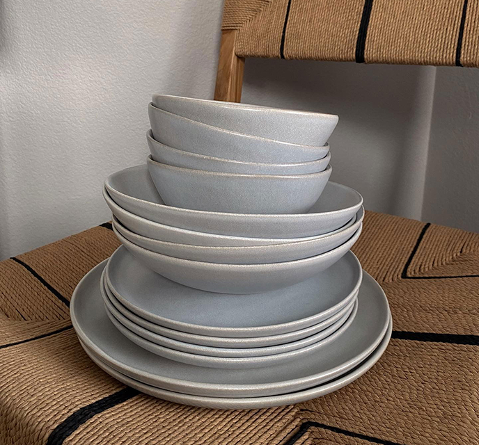Stack of stone blue ceramic bowls and plates on a woven chair.