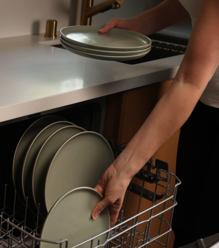 Person loading plates into a dishwasher rack in a kitchen.