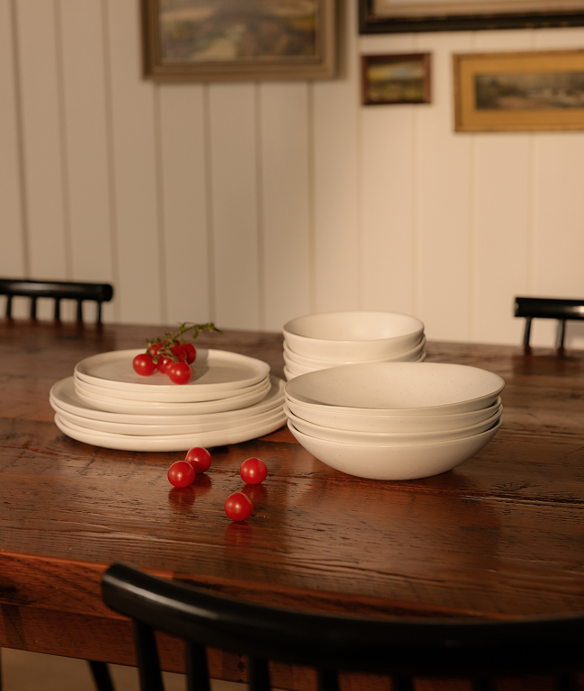 Stacked white plates and bowls with cherry tomatoes on a wooden table.