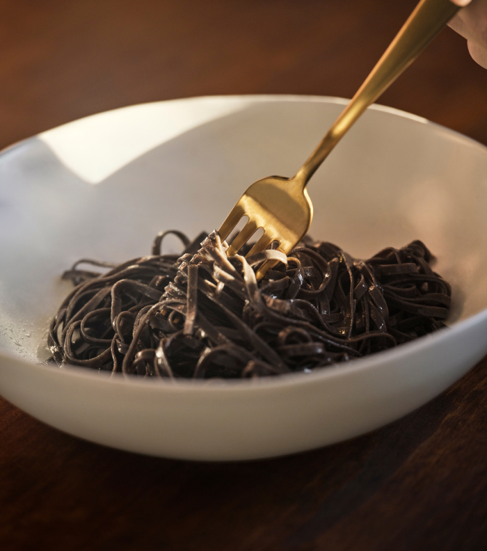 A fork twirling black pasta in a white bowl.