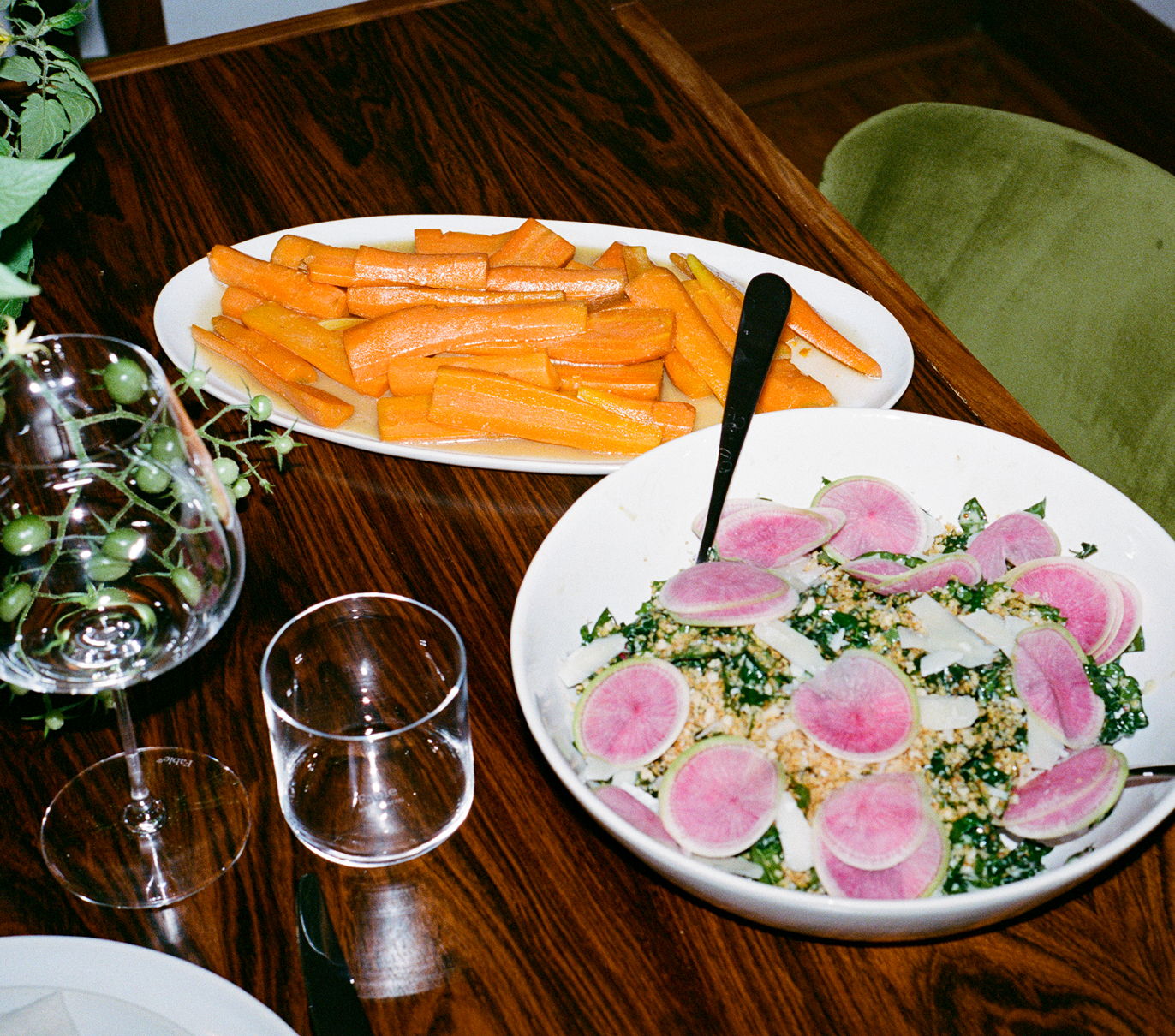 Dishes of sliced carrots and a salad with pink radishes on a wooden table.