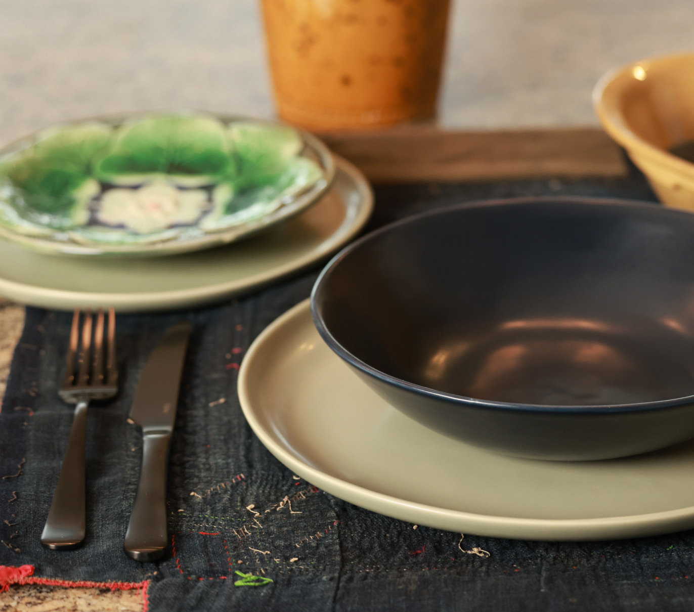 Table setting with plates, bowl, fork, and knife on a dark cloth.