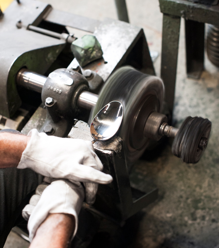 Person polishing a spoon with a machine, wearing white gloves.