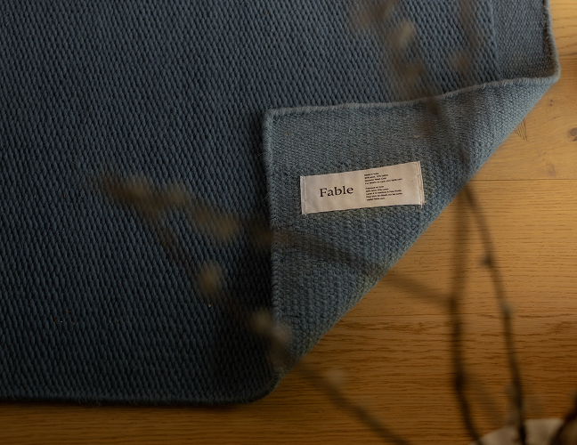 Blue textured fabric with a label reading 'Fable' on a wooden surface.