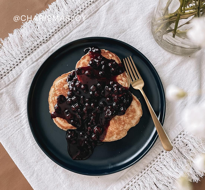 Pancakes topped with berry sauce on a dark plate with a fork.