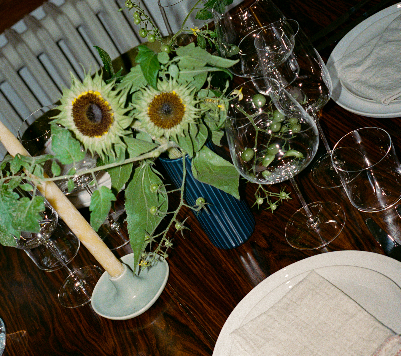 Sunflowers in a vase on a dining table with glasses and plates.