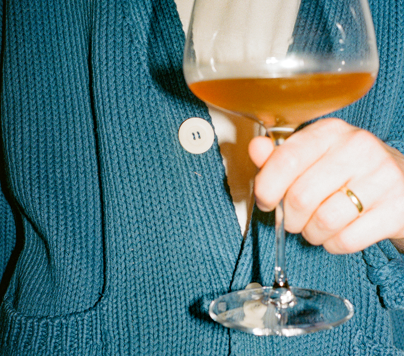 Person holding a wine glass wearing a blue knitted sweater.
